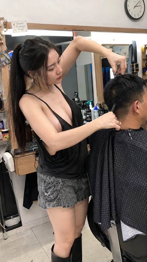 A woman in a dark sleeveless top trims the hair of a seated client in a salon.